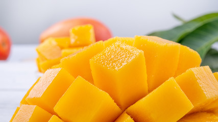 Fresh mango,beautiful chopped fruit with green leaves on bright wooden table background. Tropical fruit design concept, close up, copy space.