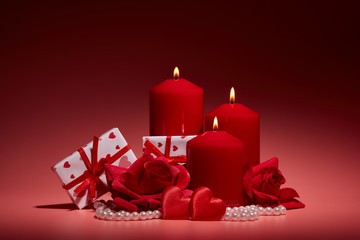 Still life with gift boxes, burning candles, red roses and hearts on red background. Valentine's day. Wedding day