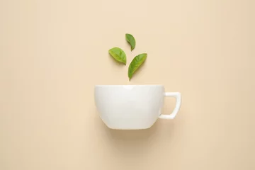Poster Fresh tea leaves and cup on beige background, top view © New Africa