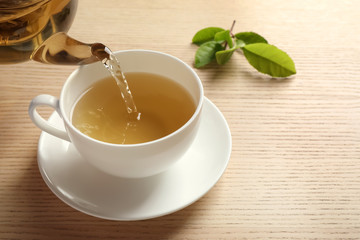 Pouring green tea into cup on wooden table. Space for text