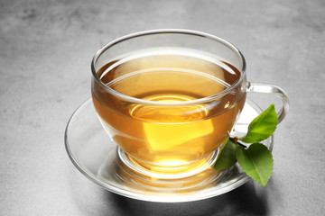 Cup of green tea and leaves on grey table