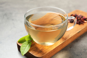 Cup of green tea and leaves on grey table, closeup