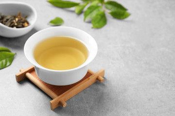 Cup of green tea, dry and fresh leaves on grey table. Space for text