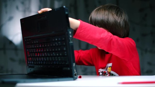A boy sits at a table examines the back of a laptop.