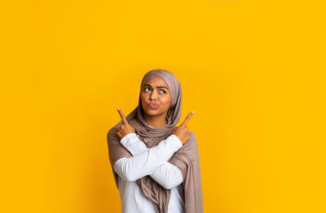 Doubtful black muslim girl pointing at copy space with crossed hands