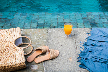 Summer background with straw hat, flip flops, wicker bag, blue pareo and orange fresh juice near the swimming pool. Summer holiday trendy concept. Top view.