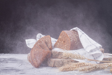 Sliced bread with seeds in flour snowstorm. Ears and wooden cuts in black studio. Food theme.