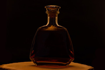Bottle of alcohol in muted light. Wooden stand and dark background. Alcoholc concept.