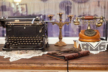 Fototapeta na wymiar Vintage antique phone, typewriter and candlestick on the table