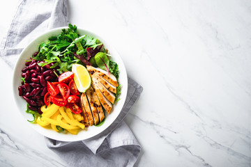 Healthy salad buddha bowl plate with cherry tomatoes, chicken, beans, sweet pepper, lime and mixed greens on marble background top view. Healthy food. Superfood meal.	