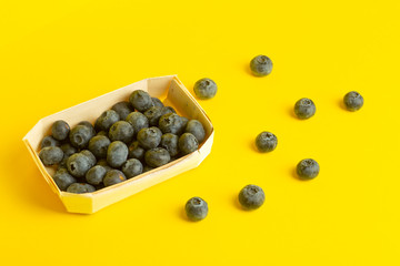 Blueberry berries on a yellow background. A scattering of berries on a colored yellow background. Minimal food and summer concept