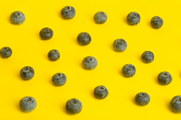 Blueberry berries on a yellow background. A scattering of berries on a colored yellow background. Minimal food and summer concept