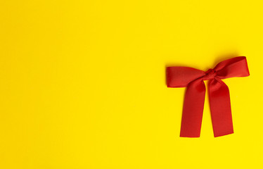 Gift bow on a yellow background. Red gift bow with shadow on a colored yellow background. Gift concept. Minimal copy space