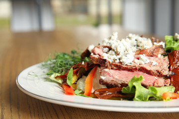 Delicious salad with roasted meat and vegetables served on wooden table indoors, closeup
