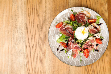 Delicious prosciutto salad with vegetables served on wooden table, top view. Space for text
