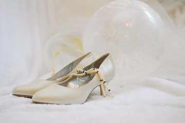 Women's beige or ivory shoes, next to beads and a balloon