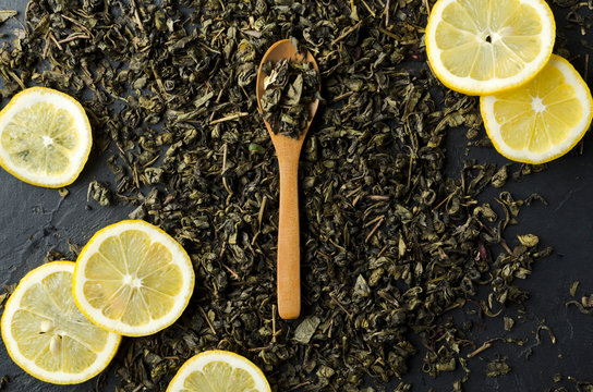 Closeup of lemon slices, wooden spoon full of dery tea leaves, hipe of dery tea on the dark table