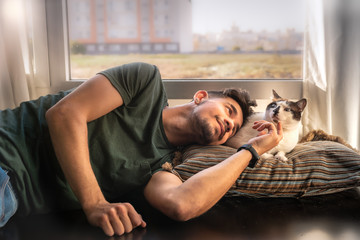 hombre joven se acuesta junto a gato blanco y negro y acaricia su cabeza