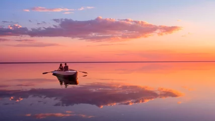 Poster de jardin Corail Un couple amoureux regarde le magnifique coucher de soleil dans un bateau à rames sur le lac. Ciel rose et nuages vanille. Scène romantique - les amoureux montent un bateau dans la nature pendant le coucher du soleil. Paysage incroyable avec des gens