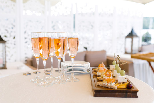 Glasses of pink champagne stand on the buffet table next to a plate of appetizers