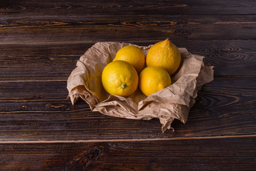 Four fresh lemons on wooden table. Citrus fruits in kraft paper. Organic fruits concept.