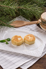 Cottage cheese pancakes with sour cream on white plate on wooden table