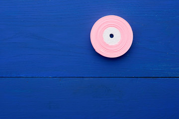 one round bobbin with pink ribbon on a blue wooden background