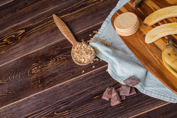 Organic food background. Bananas, spoon with oatmeal flakes, chololate and cookies on wooden table. Healthy eating concept.