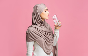 Muslim woman in headscarf drinking clean mineral water over pink background