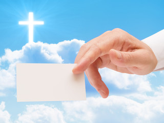 Religious man hand presenting blank white card against cloudy sky with illuminated cross