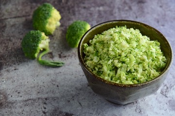Raw organic broccoli rice in a bowl on grey background