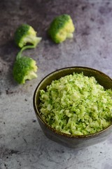 Raw organic broccoli rice in a bowl on grey background