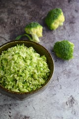 Raw organic broccoli rice in a bowl on grey background