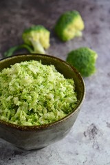 Raw organic broccoli rice in a bowl on grey background