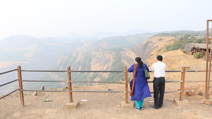 Fototapeta na wymiar Lonavala, Maharastra/India- January 12 2019: A married couple looking at the valley from behind the railing. Holiday destinations in India.