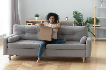 African woman sitting on couch unpacking received parcel feels happy