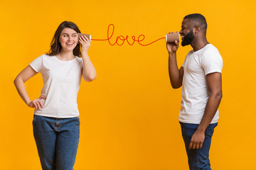 Romantic multiracial couple talking sweet through tin phone