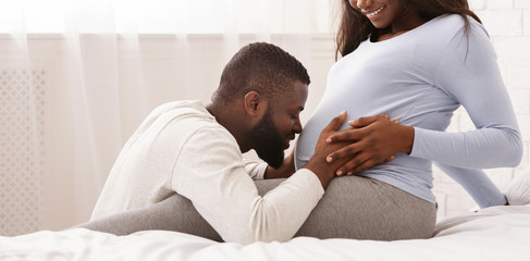 Black man hugging his pregnant wife tummy and kissing it - Powered by Adobe