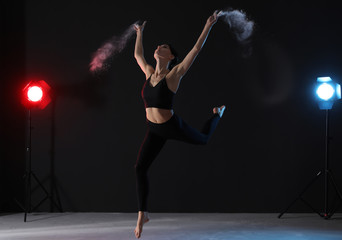 Professional acrobat with chalk powder exercising in dark studio