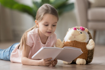 Cute little girl reading interesting book, lying on warm floor