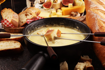 Gourmet Swiss fondue dinner on a winter evening with assorted cheeses on a board alongside a heated pot of cheese fondue with two forks dipping