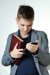 Portrait of a teenage boy on a gray background with a smartphone and a book. Concept - teenagers are more interested in smartphones than books