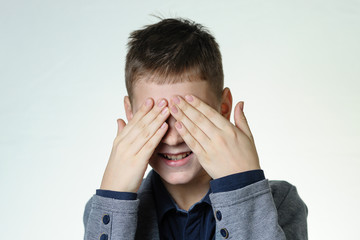 Portrait of a teenage boy on a gray background, closed his eyes with his hands. Concept - unwillingness to see something