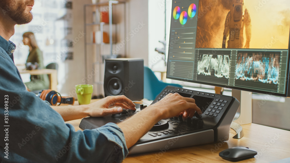 Poster male video editor with beard and jeans shirt works with footage on his computer using an editing con