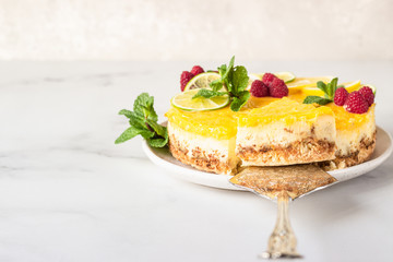 Lemon mousse vanilla cheesecake with lemon curd decorated by lemon and lime slices, frozen raspberry and mint. Light grey background.