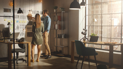 Young Creative Male and Female are Organizing a Mood Board on a Wall of Their Cool Office Loft....