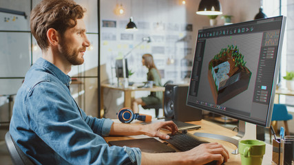 Obraz premium Beautiful Male Working in an Urbanistic Programm Creating 3 visualisation on His PC with Big Display. He Works in a Cool Office Loft. Other Female Creative Colleague Works in the Background.