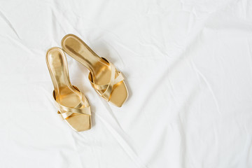 Gold female slippers shoes on white linen. Minimal flat lay fashion composition. Top view glamour accessory concept.