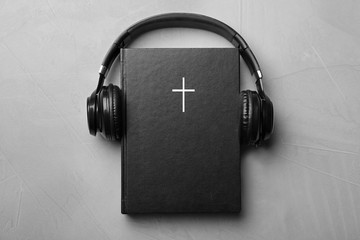 Bible and headphones on light grey background, top view. Religious audiobook