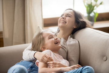 Happy mother and laughing little daughter relaxing on couch together